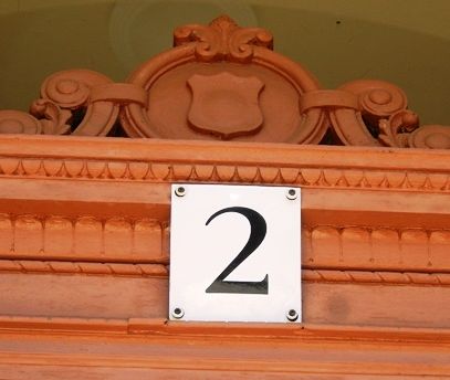 Hausnummer „2“ auf verziertem, terrakottafarbenem Holzzierrat.