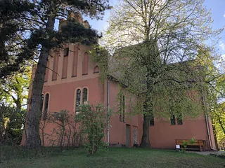 Historische, terrakottafarbene Kirche, umrahmt von großen Bäumen.