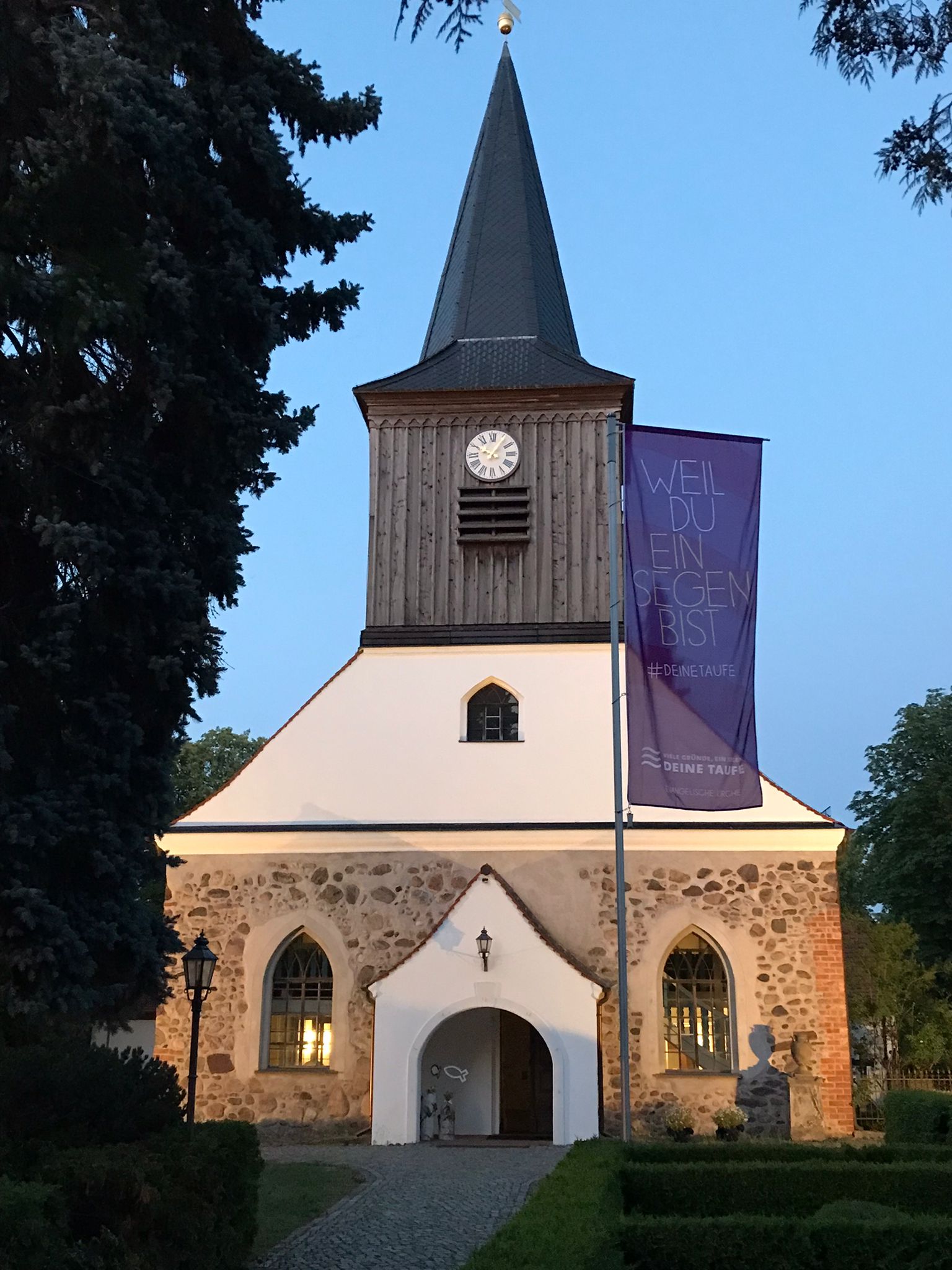 Historische Kirche bei Dämmerung mit blauem Banner für die Taufe.