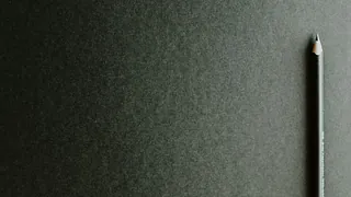 Angespitzter Bleistift auf dunklem Papier, symbolisiert Studium. 