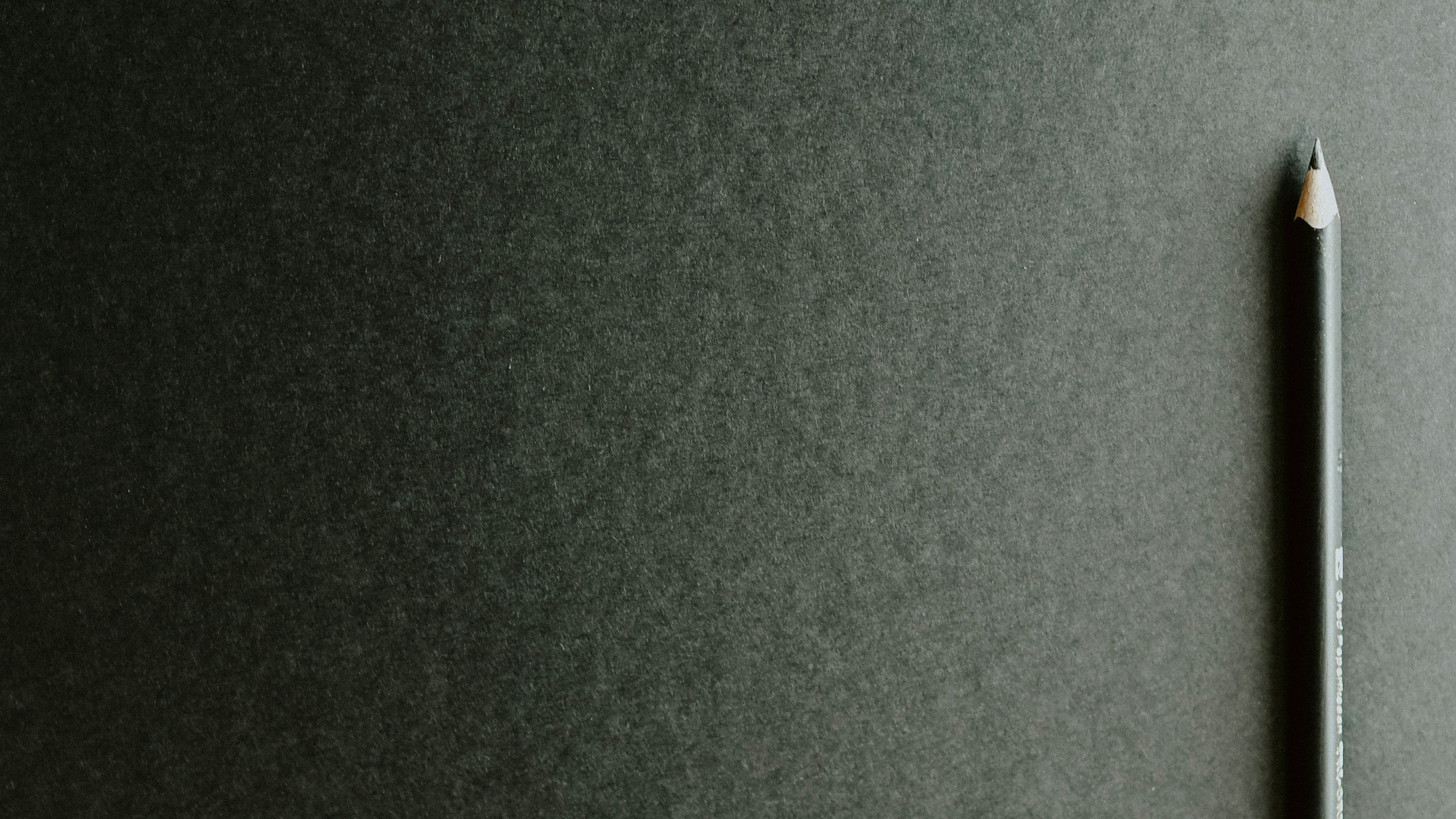 Angespitzter Bleistift auf dunklem Papier, symbolisiert Studium. 