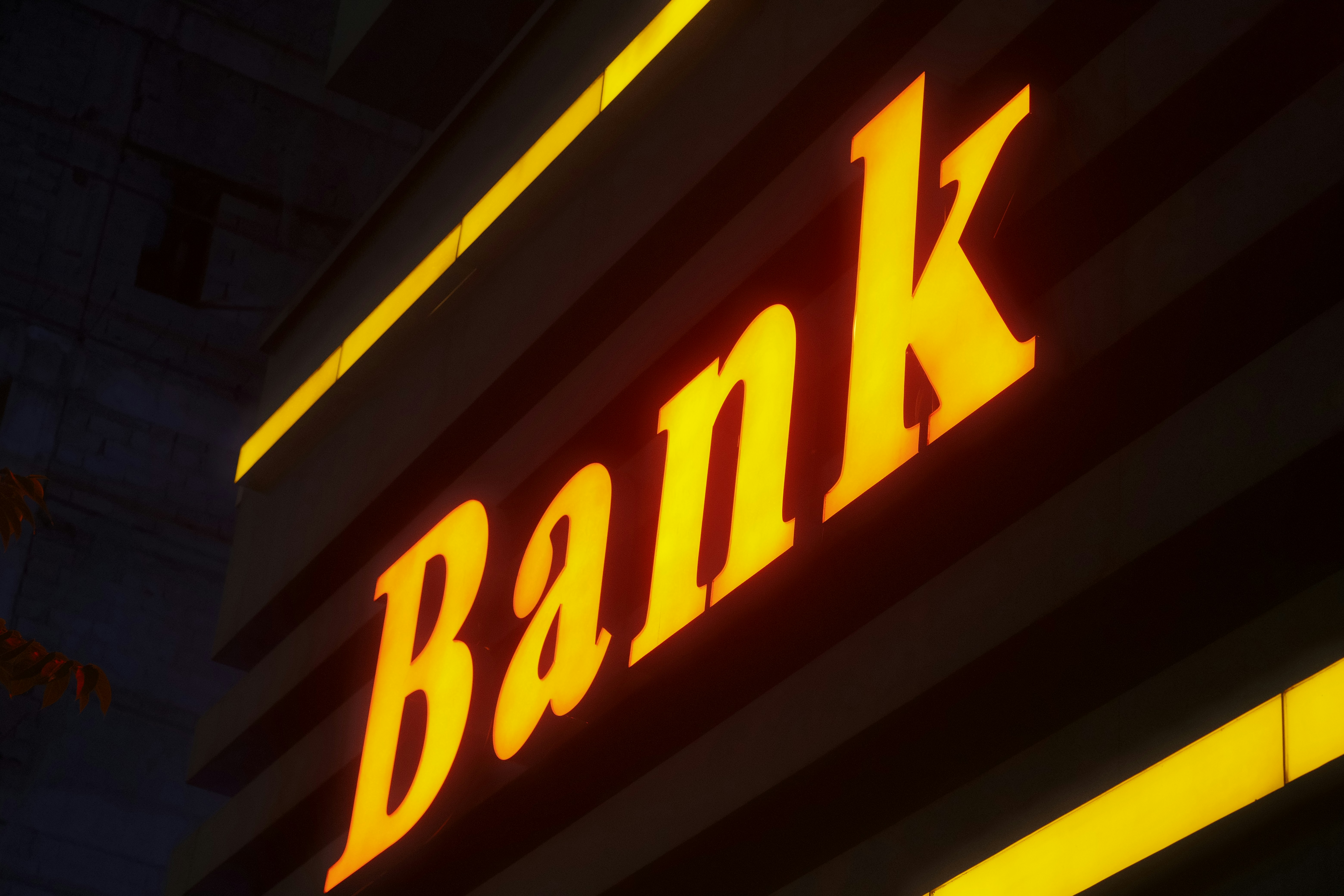 Helles gelbes Neonschild mit dem Wort „Bank“ bei Nacht.